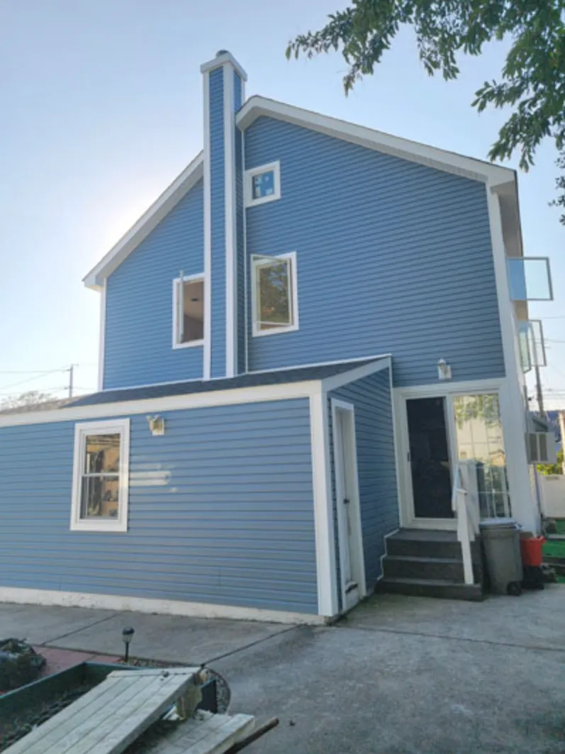 Rear of a house finished in blue siding with new windows and door