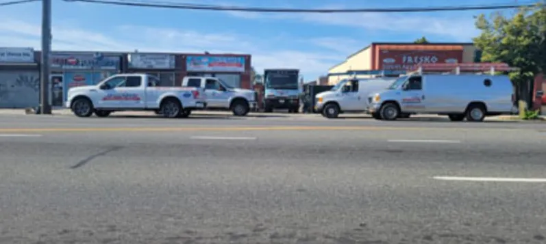 Row of white JC and Son pickup trucks, vans and a box truck parked along a commercial street