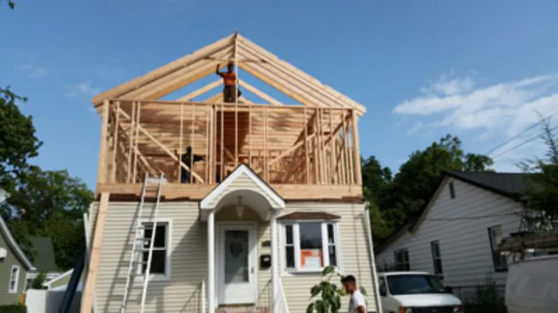 Carpenter framing the walls and gable of a second-story addition on a Cape-style house
